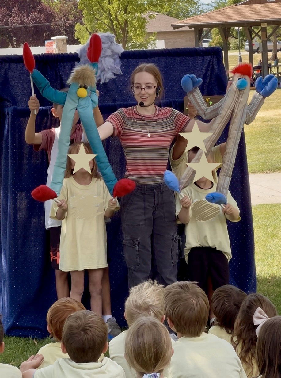 A puppeteer and young helpers holding up long-armed puppets at an outdoor summer show